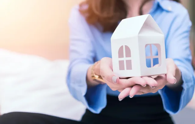 Representación de mujer con una casa en las manos.